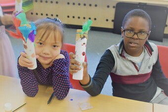 Two children hold up homemade kazoos made from decorated cardboard tubes