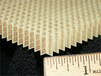 Photo of a split ring resonator array metamaterial with a ruler showing the size of the component units approximately one eighth of an inch.
